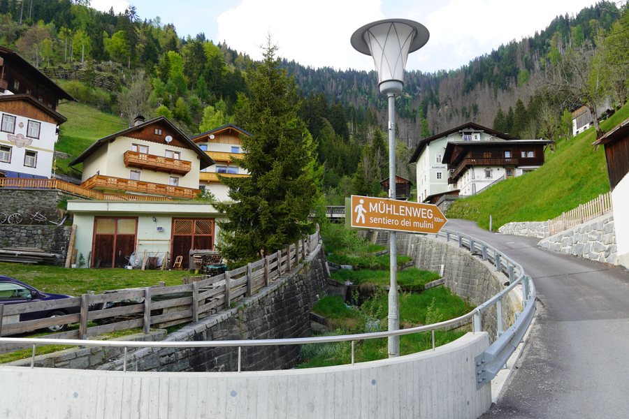Wegweiser zum Mühlenweg neben einem Bach zwischen Häusern im Lesachtal
